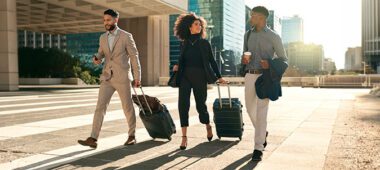 Three business professionals walking with suitcases through a modern business district during a corporate relocation.